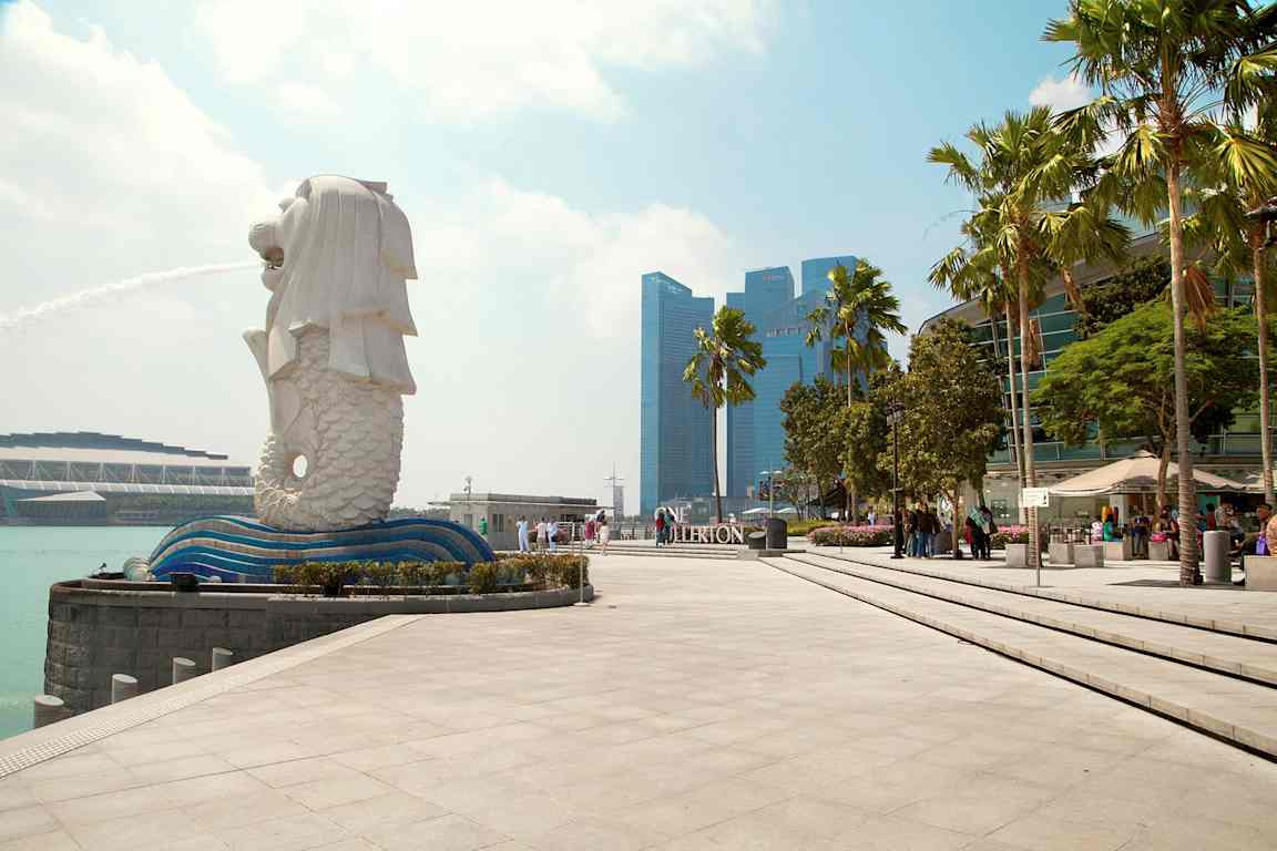 Kuva Merlion-patsasta Singaporessa suihkulähteen kanssa, ympärillä modernia arkkitehtuuria ja palmuja. (Tekoälyn luoma teksti)