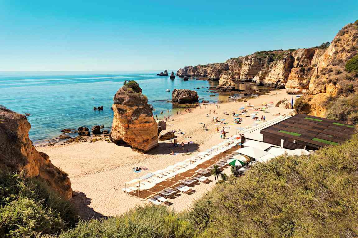 Hiekkaranta aurinkotuoleineen ja päivänvarjoineen, jota ympäröivät kalliot ja tyyni meri. (Tekoälyn luoma teksti)