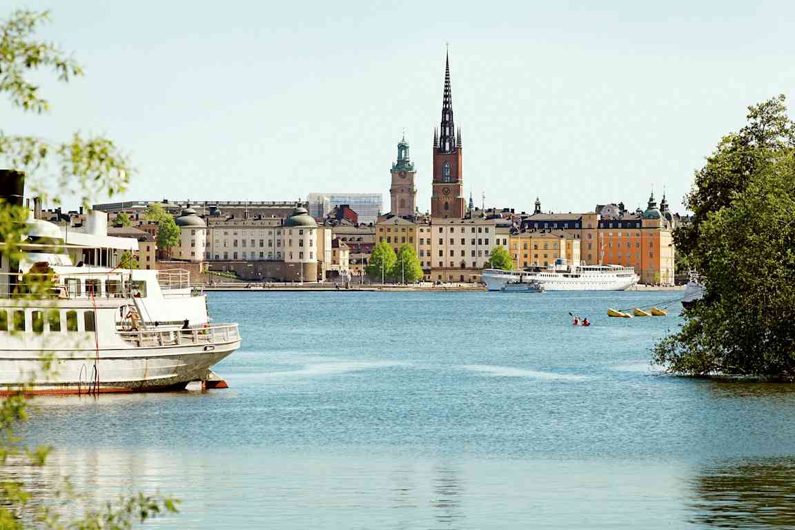 Kaupunkinäkymä, jossa rakennuksia, vettä ja kirkko, jossa on korkea torni, nähtynä veden ääreltä. (Tekoälyn luoma teksti)