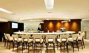 Moderni baaritiski, jota ympäröivät tuolit. Yksi henkilö seisoo tiskin takana. (Tekoälyn luoma teksti)