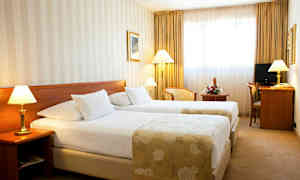 Hotellihuone, jossa on kaksi yhden hengen sänkyä, lamppuja sänkyjen vieressä ja kirjoituspöytä tuolilla. (Tekoälyn luoma teksti)