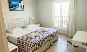 Hotellihuone, jossa on kaksi yhden hengen sänkyä, koristeltuna raidallisilla päiväpeitoilla ja pyyhkeillä. Näkyvissä on ikkuna ja kirjoituspöytä. (Tekoälyn luoma teksti)