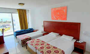 Hotellihuone, jossa on kaksi yksittäissänkyä, päivänsänky ja pöytä ikkunan luona. (Tekoälyn luoma teksti)