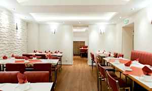 Ravintola, jossa pöydät on katettu ja punaiset tuolit. (Tekoälyn luoma teksti)