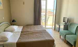 Hotellihuone, jossa on kaksi yhden hengen sänkyä, pieni TV, kaksi vihreää tuolia ja parveke näkymällä. (Tekoälyn luoma teksti)