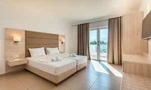 Valoisa hotellihuone, jossa kaksi vuodetta, parvekkeen ovi ja puuhuonekalut. (Tekoälyn luoma teksti)