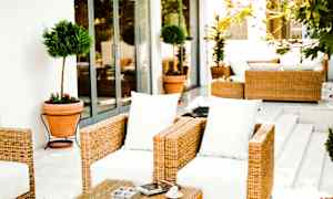 Rottinkikalusteet valkoisilla tyynyillä terassilla. (Tekoälyn luoma teksti)