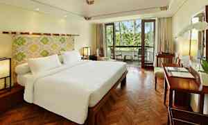 Hotellihuone, jossa on suuri parivuode, puulattia ja parveke, jolta avautuu näkymä vehreyteen. (Tekoälyn luoma teksti)