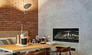 Kodikas ruokailutila, jossa on puinen pöytä, tarjotin tarvikkeineen, kaksi viinilasia ja takka taustalla. (Tekoälyn luoma teksti)