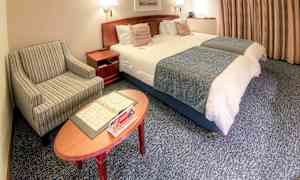 Hotellihuone, jossa on kaksi pedattua yhden hengen vuodetta, raidallinen nojatuoli ja sohvapöytä, jolla on esitteitä. (Tekoälyn luoma teksti)