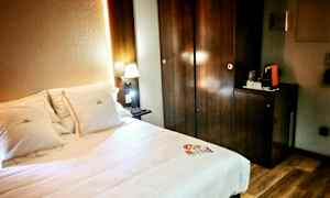 Hotellihuone, jossa sänky ja valaistu yölampu tumman puisen kaapin vieressä. (Tekoälyn luoma teksti)