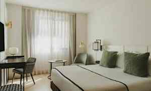 Modernisti sisustettu huone, jossa on sänky, kirjoituspöytä, tuoli ja ikkunat ohuilla verhoilla. (Tekoälyn luoma teksti)