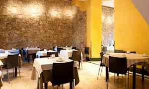 Huone, jossa on pöytiä ja tuoleja, valkoisia liinoja ja kahvikuppeja, sekä seinät kiveä ja keltaisia yksityiskohtia. (Tekoälyn luoma teksti)