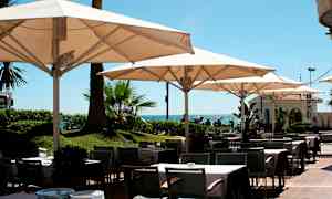 Ulkoterassiravintola, jossa pöytiä, tuoleja ja aurinkovarjoja lähellä merta. (Tekoälyn luoma teksti)