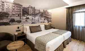 Hotellihuone, jossa on parivuode, kaksi tyynyä, moderni sisustus ja seinässä kaupunkimaisemaa esittävä valokuvatapetti. (Tekoälyn luoma teksti)