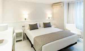 Valoisa ja moderni hotellihuone, jossa on leveä sänky, kaksi yöpöytää ja nojatuoli ikkunan vieressä. (Tekoälyn luoma teksti)