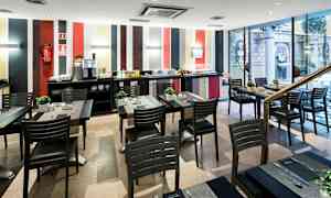 Ruokasali, jossa on useita pöytiä ja tuoleja, moderni sisustus ja buffettialue takaseinällä. (Tekoälyn luoma teksti)