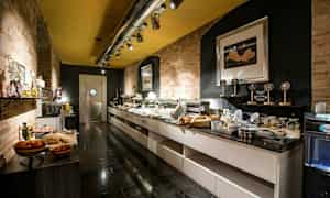 Buffetalue, jossa on ruokaa ja juomia useilla tasoilla, ympärillä tiiliseinät ja moderni valaistus. (Tekoälyn luoma teksti)