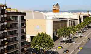 Katu, jolla on puita ja ajoneuvoja suurten rakennusten edessä, mukaan lukien rakennus, jossa on kyltti 'Fira de Barcelona'. (Tekoälyn luoma teksti)