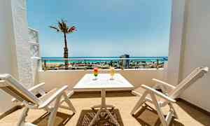 Terassi, jossa kaksi valkoista tuolia ja pöytä, kaksi juomaa sekä näkymä rannalle ja merelle. (Tekoälyn luoma teksti)