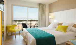 Hotellihuone, jossa kaksi sänkyä, tuoli ja parveke näkymällä. (Tekoälyn luoma teksti)