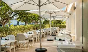 Ulkojäterassi, jossa valkoiset pöydät ja tuolit sekä valkoiset päivänvarjot. (Tekoälyn luoma teksti)