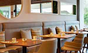 Moderni kahvila, jossa on puupöytiä, tuoleja ja sohvia. Pöydillä on kuppeja ja pieniä kulhoja. (Tekoälyn luoma teksti)