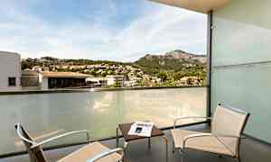 Parveke, jossa on kaksi tuolia, pöytä ja lasiseinä, jolta avautuu näkymä vuoristoiseen ja kaupunkimaiseen ympäristöön. (Tekoälyn luoma teksti)