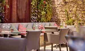 Ulkotila, jossa istuimia ja koristeltuja seiniä, ympäröitynä vihreällä kasvillisuudella. (Tekoälyn luoma teksti)