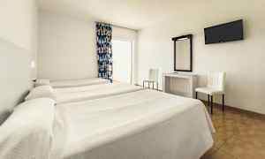 Hotellihuone, jossa on kolme yhden hengen sänkyä, työpöytä peilillä, kaksi tuolia ja seinään kiinnitetty televisio. (Tekoälyn luoma teksti)