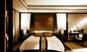 Nykyaikainen makuuhuone, jonka keskellä on suuri sänky, ympäröitynä tyylikkäillä tummilla puupaneeleilla ja lämpimillä valonlähteillä. (Tekoälyn luoma teksti)