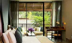 Hotellihuone, jossa on sänky ja pieni kirjoituspöytä sekä terassi istuimineen ja näkymä vehreyteen. (Tekoälyn luoma teksti)