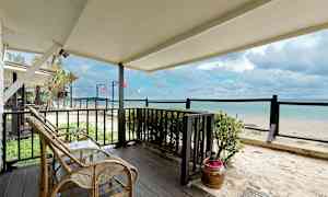 Näkymä terassilta, jossa on rottinkikalusteet, hiekkarannalle ja merelle. (Tekoälyn luoma teksti)