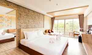 Tilava hotellihuone, jossa on iso sänky, hiekkakiviseinä, peili, sohva ja parvekkeelle johtava ikkuna. (Tekoälyn luoma teksti)