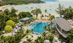 Näköala lomakohteeseen, jossa on suuri uima-allas, ympäröitynä vehreydellä ja palmuilla. Taustalla on ranta ja lahti, johon on ankkuroitu purjeveneitä. (Tekoälyn luoma teksti)