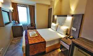 Hotellihuone, jossa pedattu parisänky. Huoneessa on kirjoituspöytä, tuoli ja verhoilla varustettu ikkuna. (Tekoälyn luoma teksti)