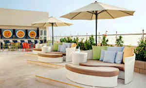 Terassi, jossa on moderneja istuinryhmiä, aurinkovarjoja ja koristeltu baari taustalla. (Tekoälyn luoma teksti)