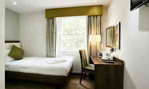 Hotellihuone, jossa yksittäinen vuode, ikkuna, kirjoituspöytä ja tuoli. (Tekoälyn luoma teksti)