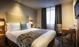 Hotellihuone, jossa on suuri sänky, työpöytä ja tuoli. (Tekoälyn luoma teksti)