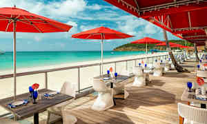 Ulkoilmaravintola punaisia aurinkovarjoja hiekkarannalla. (Tekoälyn luoma teksti)