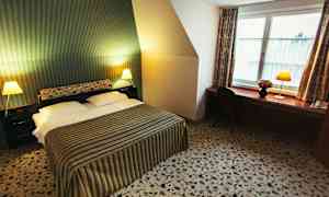 Hotellihuone, jossa on parivuode, raidallinen päiväpeitto, kaksi yöpöytää lampuilla ja työpöytä tuoleineen ikkunan vieressä. (Tekoälyn luoma teksti)