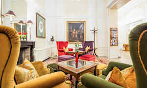 Tyylikäs oleskelutila, jossa on värikkäitä nojatuoleja ja sohvia pöydän ympärillä. Seinät on koristeltu taiteella ja sivussa näkyy takka koristeineen. (Tekoälyn luoma teksti)