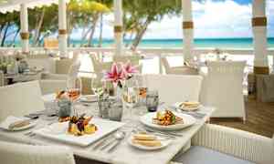 Kattaus ravintolapöydässä rannan lähellä, lautasia, laseja ja kukkia. (Tekoälyn luoma teksti)