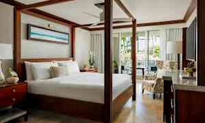 Tyylikäs makuuhuone, jossa on pylvässänky, istuimet ja näkymät vihreään luontoon avautuvien lasiovien kautta. (Tekoälyn luoma teksti)