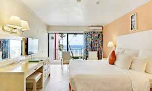 Hotellihuone, jossa suuri sänky, työpöytä, tuolit ja parveke merinäköalalla. (Tekoälyn luoma teksti)