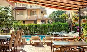 Ulkokalusteet ja aurinkotuolit uima-altaan vieressä, ympärillä vehreyttä ja rakennuksia. (Tekoälyn luoma teksti)