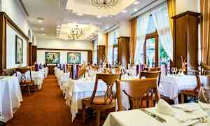 Ravintolan sisätilat, joissa on katetut pöydät ja tuolit, vaaleat verhot ja koristeelliset kattovalaisimet. (Tekoälyn luoma teksti)