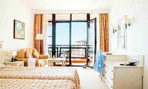 Hotellihuone, jossa kaksi erillissänkyä, sohva, työpöytä ja parveke näköalalla. (Tekoälyn luoma teksti)