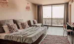 Valoisa ja moderni hotellihuone, jossa on sänky, sohva ja parveke, jossa on ulkokalusteet. (Tekoälyn luoma teksti)