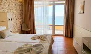 Hotellihuone, jossa on parivuode, pedattu valkoisilla lakanoilla ja koristeltu pyyhkeillä. Ikkunasta on näkymä merelle. (Tekoälyn luoma teksti)